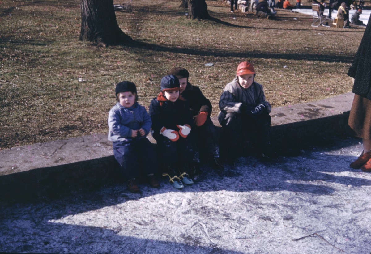 four little children sitting on a curb in winter clothes